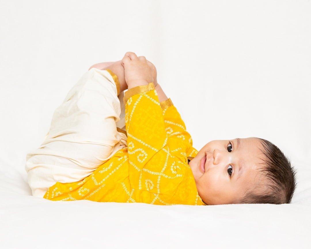 a little baby in happy baby pose in a yellow top