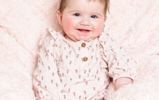 a happy baby in a pink outfit on a pink blanket