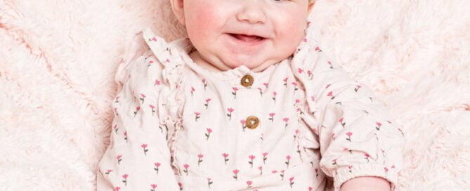 a happy baby in a pink outfit on a pink blanket