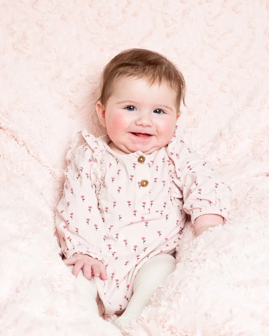 a happy baby in a pink outfit on a pink blanket