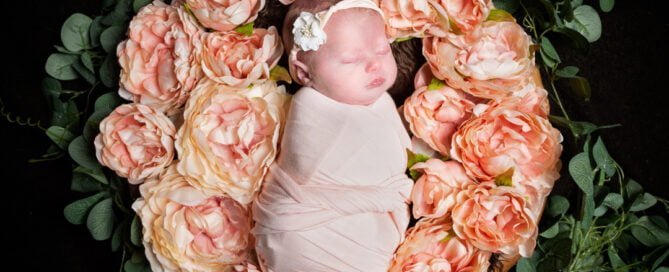 a newborn in a nest surrounded by peach peonies