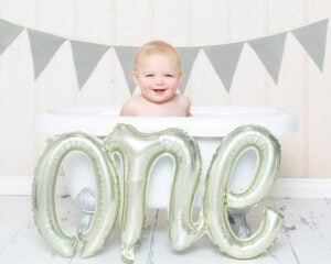 a little boy in a bath tub with a balloon that spells one 