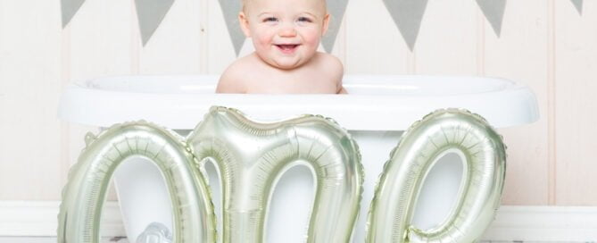 a little boy in a bath tub with a balloon that spells one