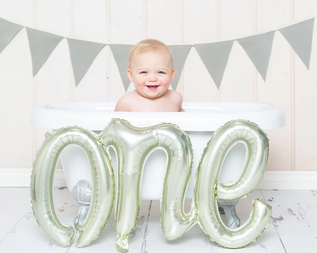 a little boy in a bath tub with a balloon that spells one