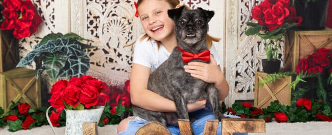 a girl poses with her dog in a red bow tie