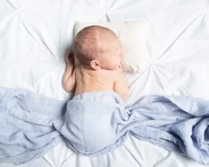 a newborn sleeps on their front on a white bed with a blue cloth on their back