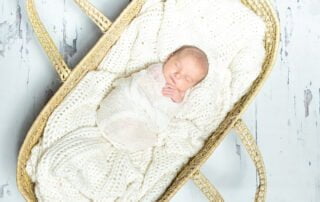 a cream lined moses basket with a sleeping wrapped newborn inside