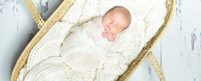 a cream lined moses basket with a sleeping wrapped newborn inside