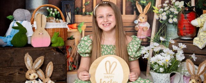 a little girl in a green dress holds a green Easter sign in a bunny themed photo shoot set