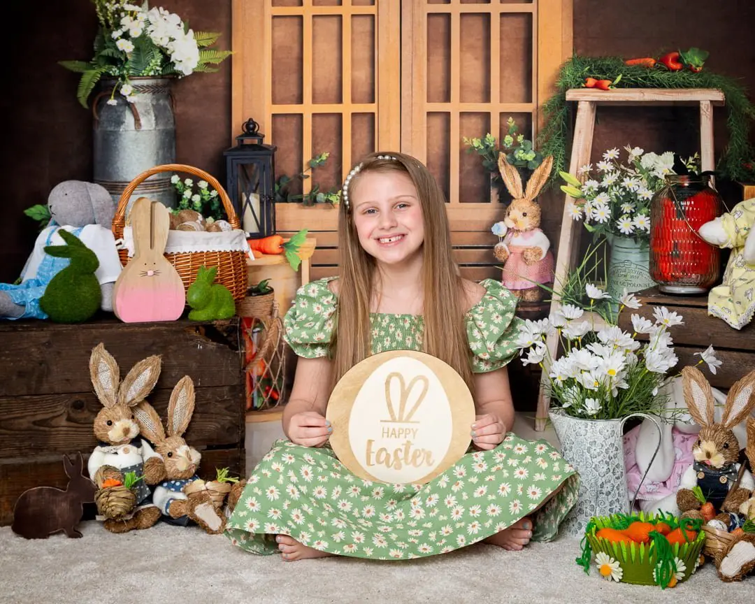 a little girl in a green dress holds a green Easter sign in a bunny themed photo shoot set