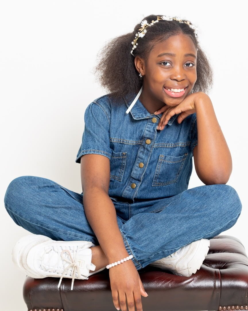 A girl in a denim jumpsuit sitting on top of a footstool