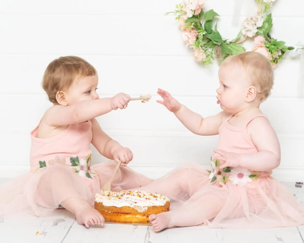 Cake Smash Photo Shoots in East Grinstead West Sussex Twin girls dressed in peach share a cake at their first birthday photo shoot
