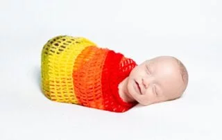 a smiling newborn wrapped in a rainbow blanket