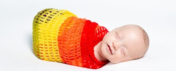 a smiling newborn wrapped in a rainbow blanket