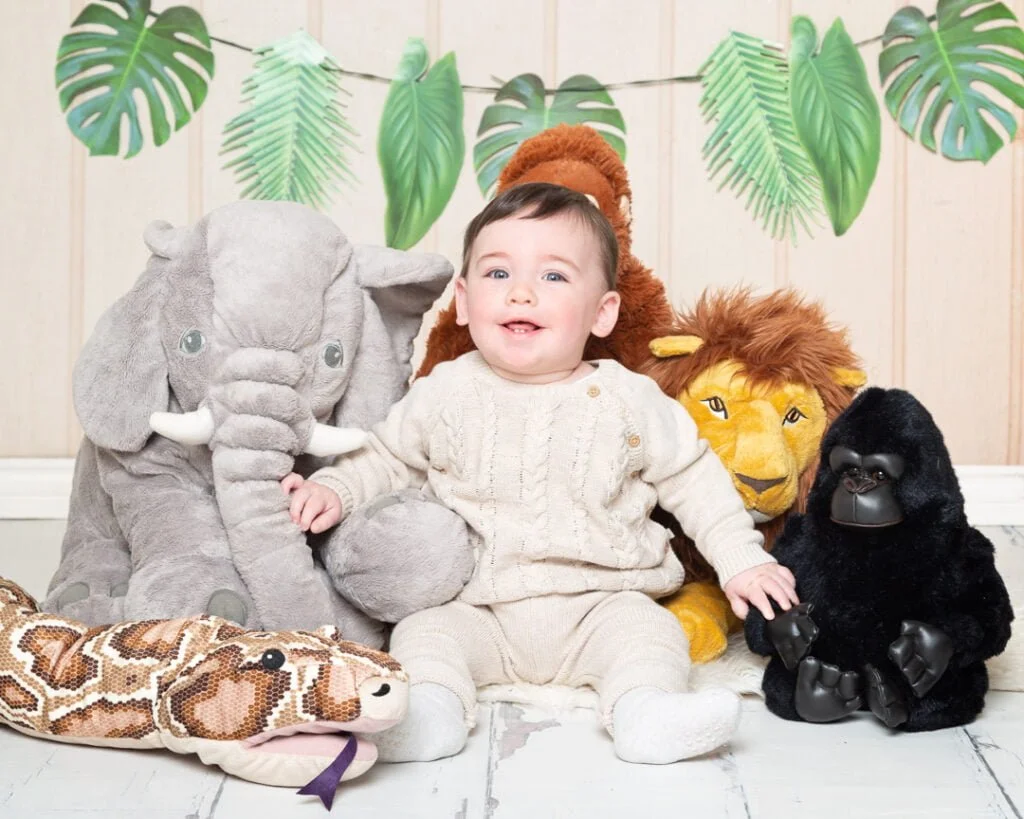 a little boy in a neutral outfit poses with jungle toys
