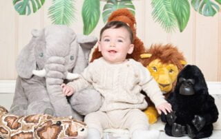 a little boy in a neutral outfit poses with jungle toys