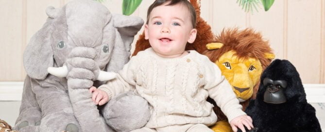 a little boy in a neutral outfit poses with jungle toys