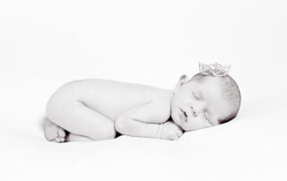 a black and white newborn image of a sleeping baby tucked up on their tummy and wearing a tiara