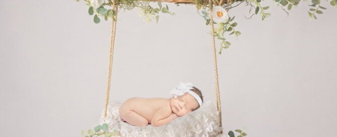 a digitally created image of a newborn on a white swing with flowers