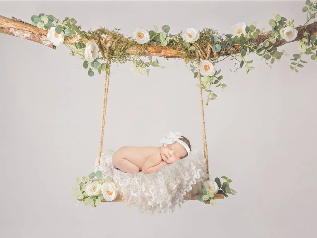 a digitally created image of a newborn on a white swing with flowers