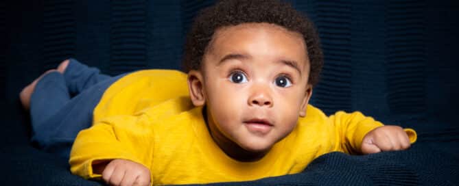 a baby poses on their tummy against a navy backdrop