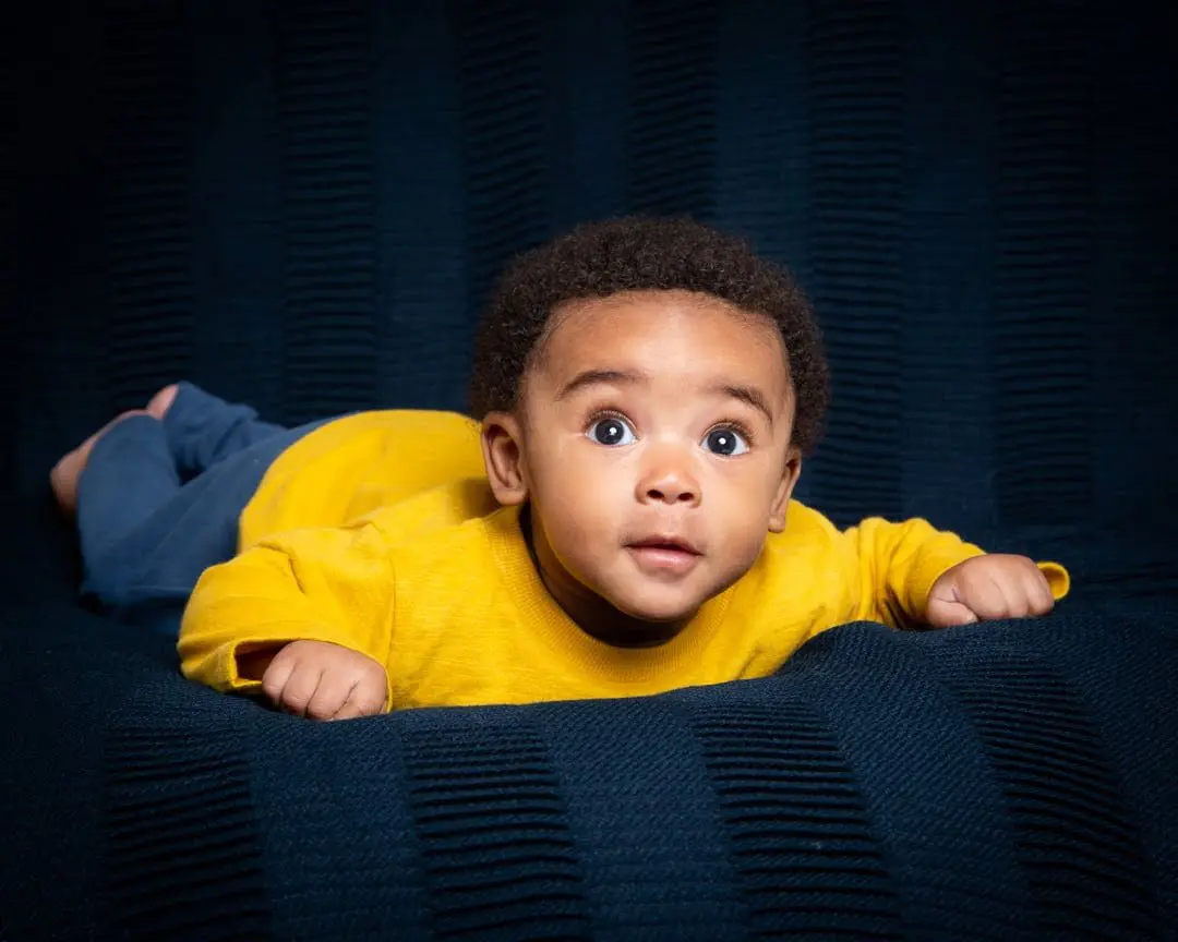 a baby poses on their tummy against a navy backdrop