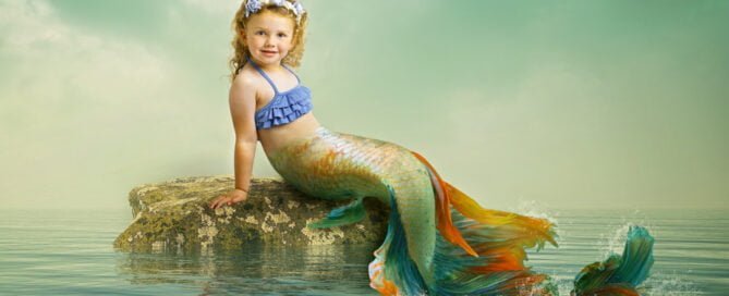a little girl sitting on a rock at a mermaid photo shoot