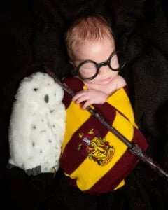 a newborn wrapped in a Gryffindor scarf wearing Harry Potter style glasses