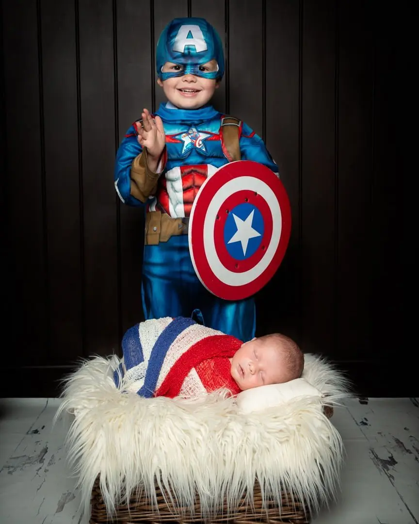 a little boy dressed as Captain America poses with his newborn brother wrapped in red, white and blue