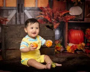 a baby poses against an autumnal background with pumpkins