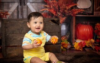 a baby poses against an autumnal background with pumpkins