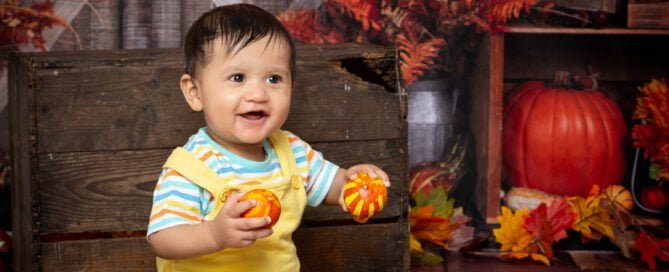a baby poses against an autumnal background with pumpkins