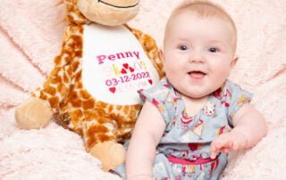 a baby sits with a personalised giraffe toy