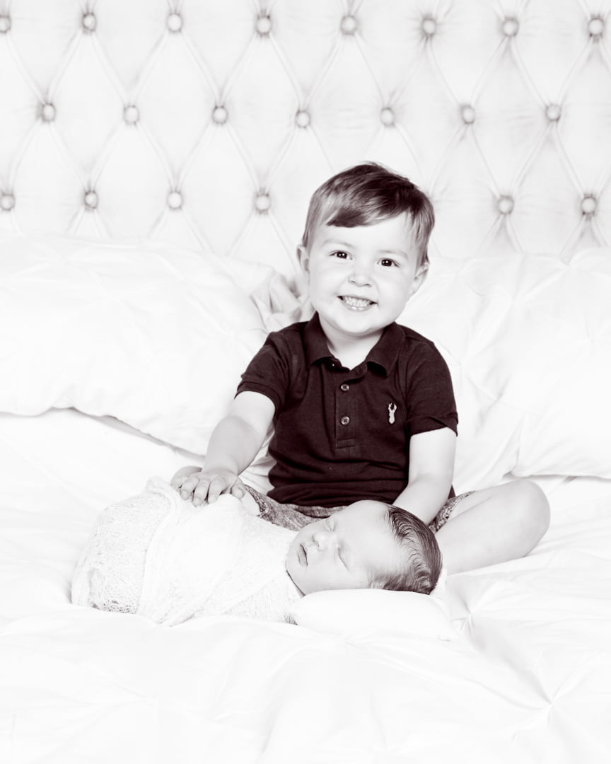 a big brother sits on a bed with his newborn sibling