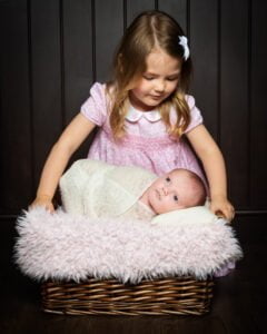 a big sister looks down at their newborn sibling swaddled in white