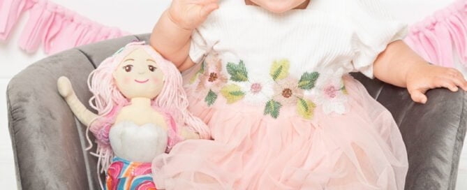 a baby in a peach dress with a mermaid soft toy