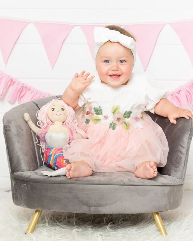 a baby in a peach dress with a mermaid soft toy