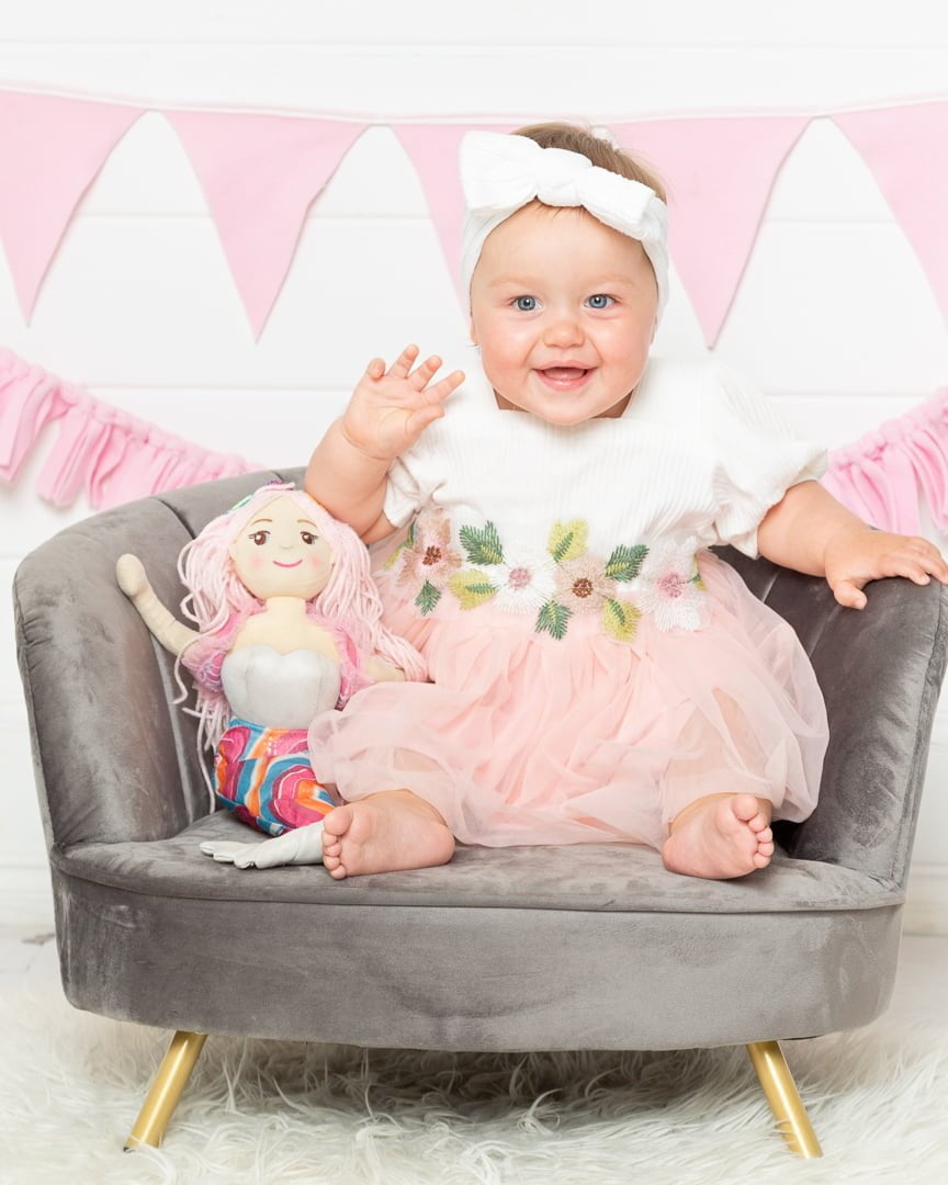 a baby in a peach dress with a mermaid soft toy
