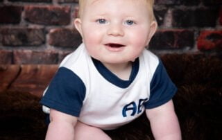 a baby poses against a brick wall backdrop in a tshirt