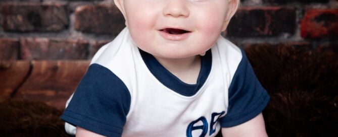 a baby poses against a brick wall backdrop in a tshirt