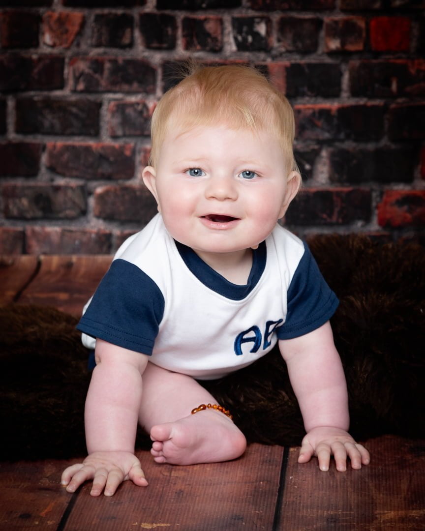 a baby poses against a brick wall backdrop in a tshirt