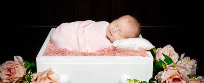 a newborn sleeping in a white drawer with peach flowers