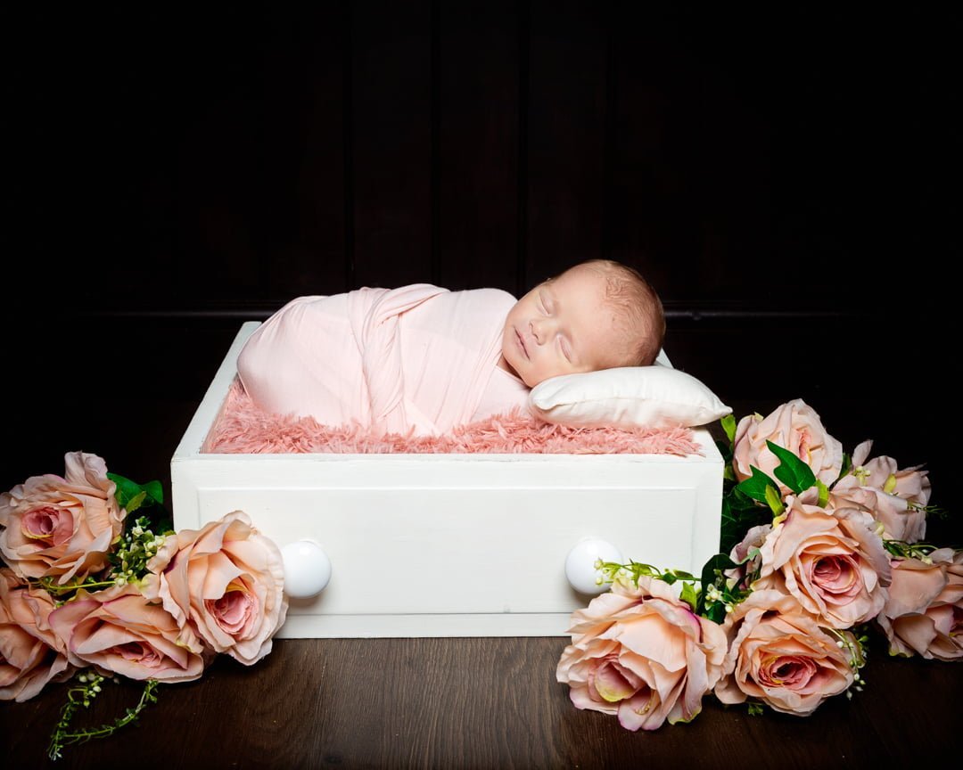 a newborn sleeping in a white drawer with peach flowers