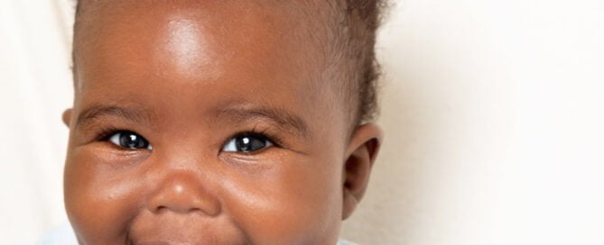 a smiling baby looks at the camera in front of a white blanket