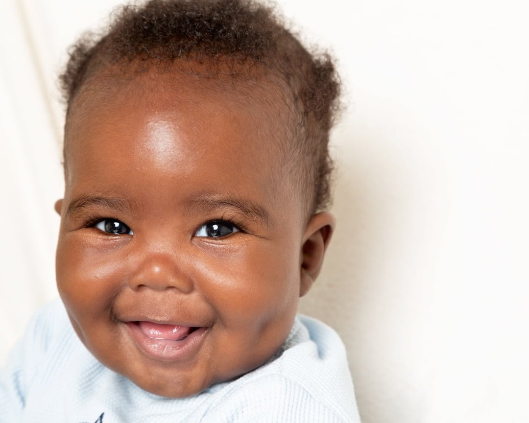 a smiling baby looks at the camera in front of a white blanket