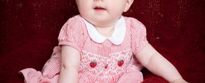 a baby in a red dress on a deep red blanket