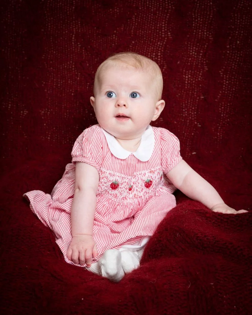 a baby in a red dress on a deep red blanket