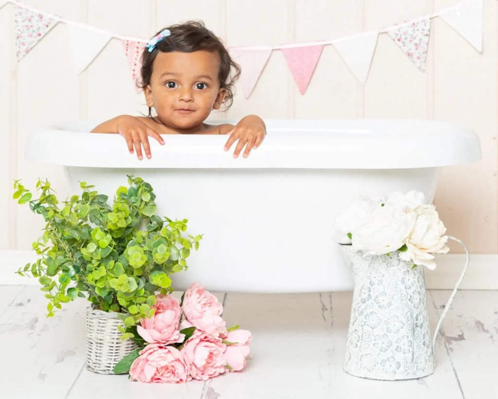 a little girl peeks over the edge of a rolltop bath with flowers in front of it
