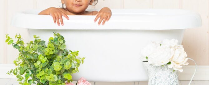 a little girl peeks over the edge of a rolltop bath with flowers in front of it