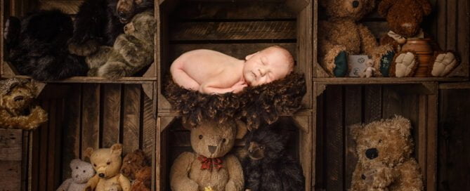 a newborn sleeping among crates of teddy bears - digital image